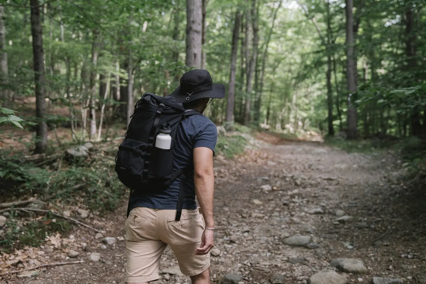 A man in a sun hat and backpack walking along a rocky forest trail